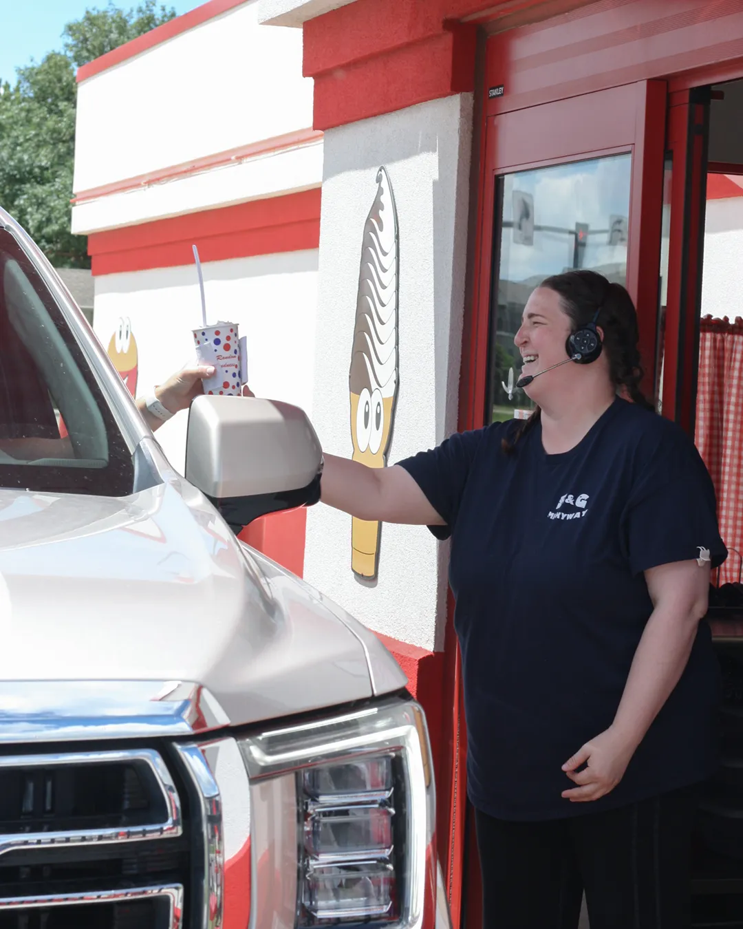 A smiling B & G Milkyway employee handing an avalanche to a customer in the drive through.